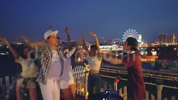 快乐的DJ在屋顶派对上与调音师合作一边欣赏音乐一边让年轻人跳舞视频的预览图