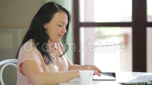 一位穿着米色上衣的年轻女子正坐在咖啡馆里在一台平板电脑上工作慢节奏视频的预览图