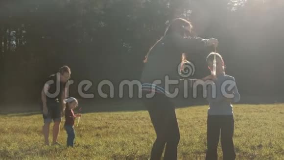 爸爸妈妈和孩子们一起玩在森林附近的草地上做肥皂泡家庭周末视频的预览图