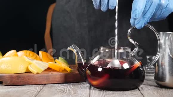 用勺子把热红酒和水果片放在茶壶里搅拌玻璃茶壶里装满了橘子和柠檬视频的预览图