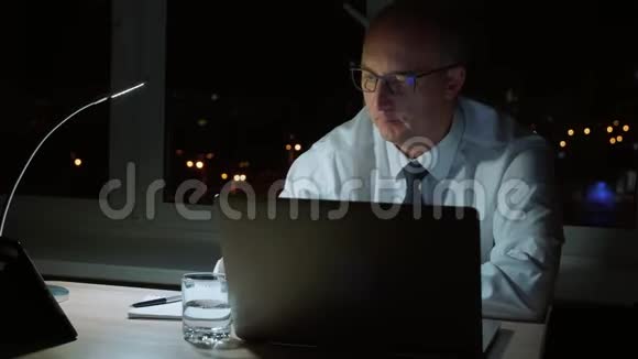 行政商人晚上坐在黑暗的办公室里打电话视频的预览图
