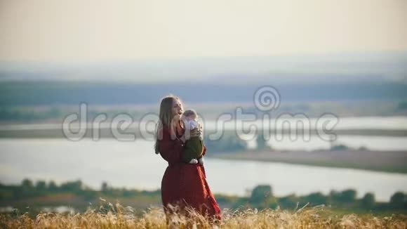 一个快乐的女人在河的背景下和她的小宝宝在田里玩耍视频的预览图