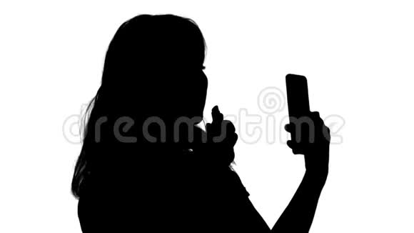 剪影金发女人涂口红在看电话视频的预览图