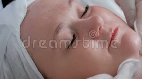 一个在美容中心的面部皮肤护理程序上闭着眼睛的胖女孩特写镜头美容师在视频的预览图