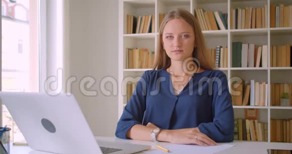 年轻漂亮的白种人女商人用笔记本电脑看着相机开心地坐在那里视频的预览图