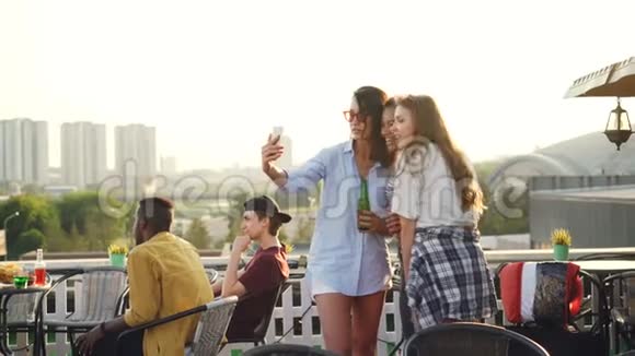 快乐的女性朋友会用智能手机自拍还会笑着站在屋顶上喝酒视频的预览图