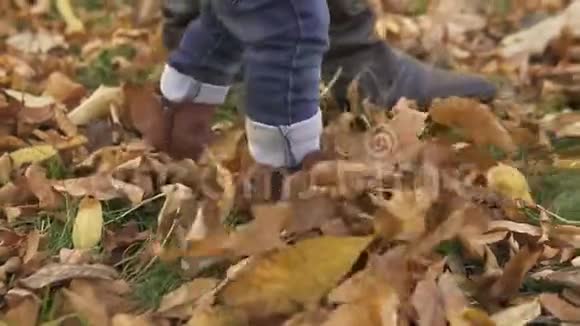 一个一岁的小男孩和他的母亲穿着棕色靴子和蓝色牛仔裤在秋天的公园里散步视频的预览图