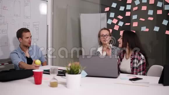 年轻的男人和两个女人坐在办公室的桌子上创造性的工作场所金发女人分享她的愿景吃人视频的预览图