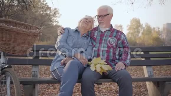 一对快乐的白人退休夫妇在阳光下坐在长凳上说话的肖像成熟的欧洲家庭视频的预览图