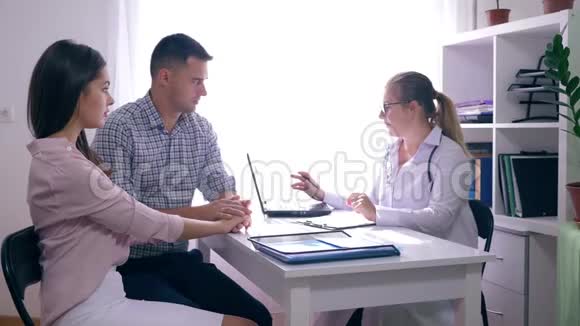 年轻的家庭医生一位医生咨询一对夫妇坐在医疗办公室的办公桌前的生育率视频的预览图