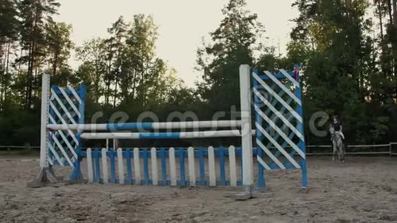 慢动作近距离低角度骑马的女孩子骑着强壮的棕色马在阳光明媚的户外沙滩跑酷里跳过篱笆视频的预览图