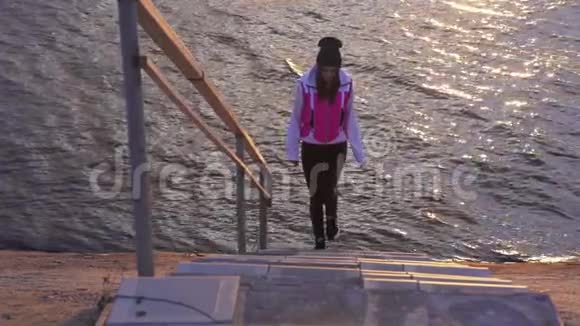 慢动作一个穿着夹克和运动裤的年轻女人从楼梯上来到一个大的湖的水上视频的预览图