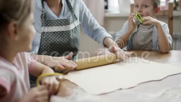 妈妈一边给孩子们讲故事一边在厨房的桌子上擀面包做饼干视频的预览图
