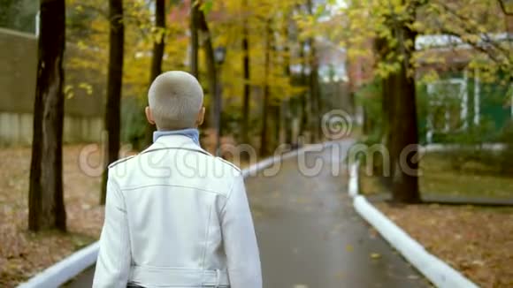时髦的金发女人留着很短的头发在秋天公园散步视频的预览图