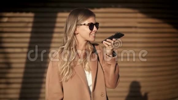 穿着外套戴着墨镜的金发女孩在秋街打电话视频的预览图