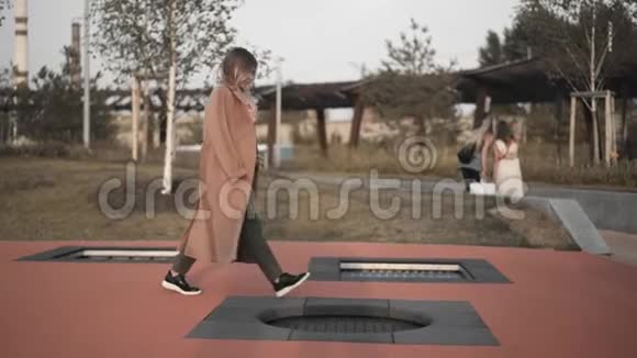 金发女人脱下外套开始跳上公园里的蹦床视频的预览图