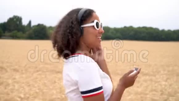 一位非洲裔美国少女少女她走在田野里用手机和无线耳机听音乐视频的预览图