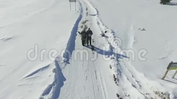 一对夫妇站在白雪皑皑的冬季道路上的鸟瞰图视频的预览图