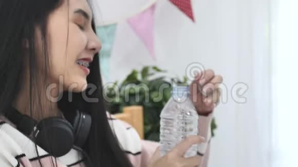 慢动作的亚洲美女从瓶子里喝水在家里很开心视频的预览图