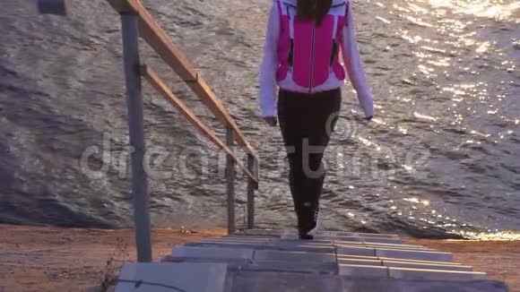 慢动作一个穿着夹克和运动裤的年轻女人从楼梯上来到一个大的湖的水上视频的预览图