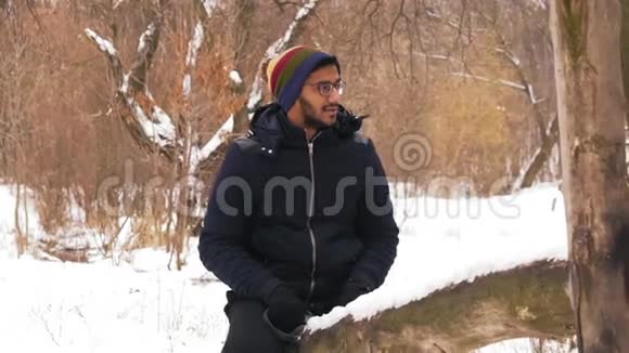 动作慢戴眼镜的印度男人在森林里的冬天骑着木秋千视频的预览图