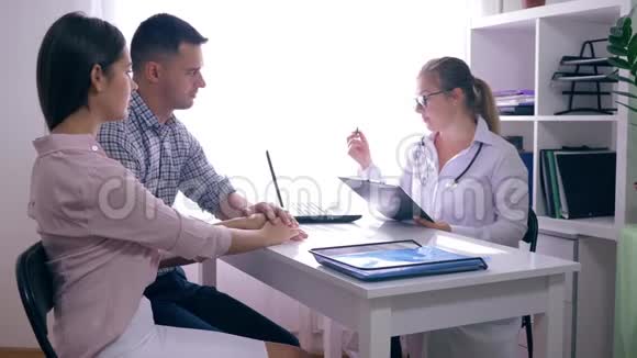 不孕不育问题一对夫妇在明亮的办公室里坐在女医生面前互相拥抱视频的预览图