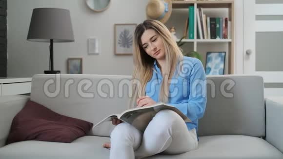 年轻女子在家看杂志坐在沙发上看时尚杂志的迷人女孩视频的预览图
