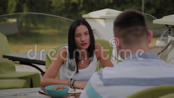 一个漂亮的女人和一个男人坐在一个开放的露台上的餐馆的桌子旁视频的预览图