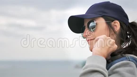 戴墨镜和帽子的徒步旅行者休闲女性在阴天享受海景的肖像视频的预览图