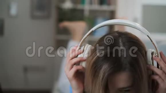 穿着蓝色服装的年轻漂亮女孩在家欣赏音乐女人从耳机里听音乐视频的预览图