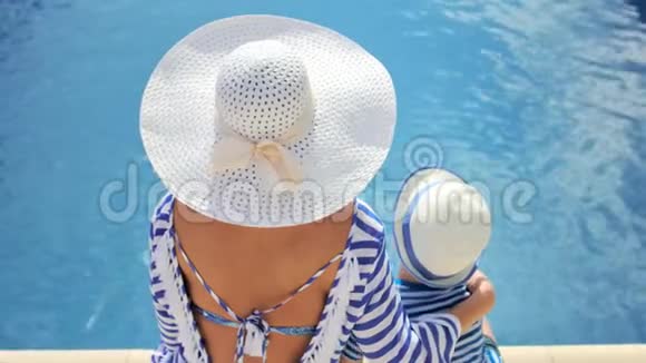 高角度后视图带帽子的母亲拥抱坐在游泳池边缘的小儿子视频的预览图