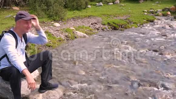 快乐的游客坐在山上湍急的河岸上的大石头上视频的预览图