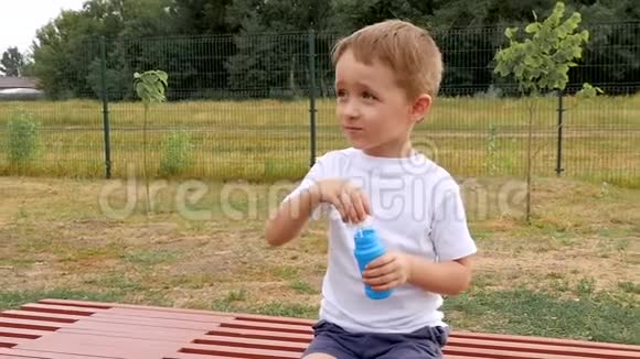 一个快乐的孩子坐在长凳上缓慢地吹泡泡视频的预览图
