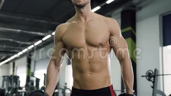 严肃迷人的男人赤裸的躯干在健身房里用哑铃锻炼视频的预览图