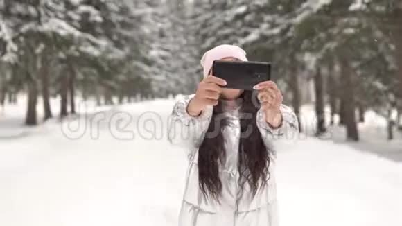 一个女孩在冬天的森林里站着用智能手机自拍4K视频的预览图