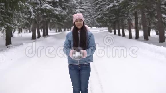 心情好的漂亮女孩站在冬天的森林里微笑着用手吹雪慢动作视频的预览图