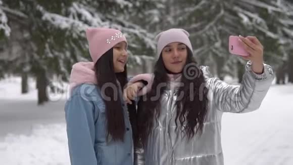 两个心情好的女朋友在冬天的森林里站着用智能手机自拍慢速高清视频的预览图