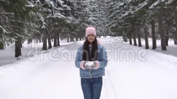心情好的漂亮女孩站在冬天的森林里用手吹雪慢速高清视频的预览图