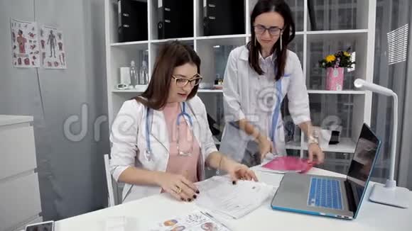 穿白色实验室外套的医生坐在工作场所看文件视频的预览图