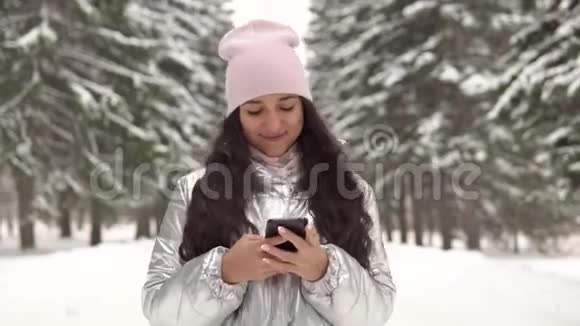 心情好的迷人女孩在冬天的森林里使用智能手机4K视频的预览图