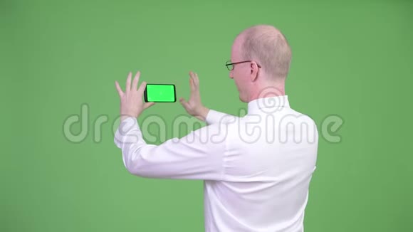 成熟秃头商人用电话拍照的后视图视频的预览图