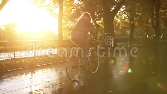 一位漂亮的女性骑着自行车在早晨的公园或林荫大道与潮湿的沥青一位年轻女子视频的预览图