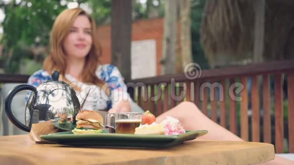阳光明媚的夏日年轻的女人在露台上喝着带糖果的茶视频的预览图