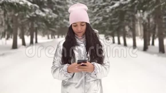 迷人的女孩穿过冬天的森林使用智能手机4K视频的预览图