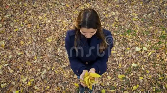 美丽的女人高兴地跳起来辗转着黄色的叶子4k60fps慢动作穿着外套的女孩在秋天散步视频的预览图