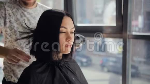 理发师用吹风机吹干女性的头发在理发后在沙龙里打盹清洁她的脖子视频的预览图