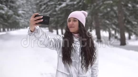 一个年轻的女孩在冬天的森林里站着用智能手机自拍慢动作视频的预览图