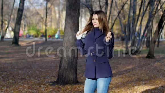 一个美丽的微笑的女人站在秋天的公园里4k每秒60帧穿外套的女孩在秋城公园里慢吞吞地走着视频的预览图