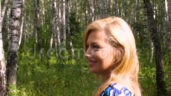 迷人的女人微笑着走在夏日公园的桦树林里纵断面图视频的预览图