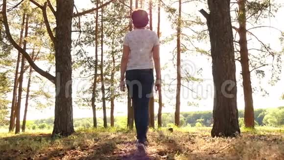 一个穿牛仔裤的年轻女人在日落的背景下穿过森林视频的预览图